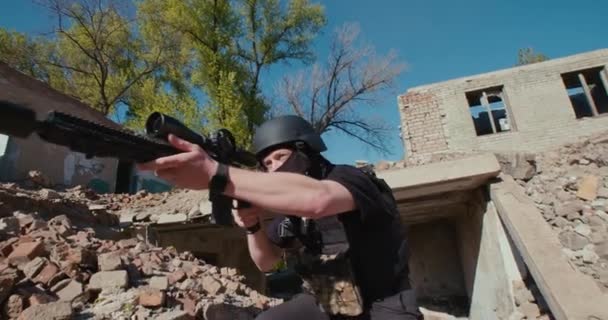 Een soldaat met een wapen verlaat het vernietigde huis en schiet. — Stockvideo