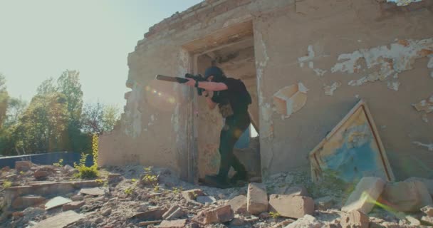 A soldier with a rifle comes out of a ruined house and aims for a shot — Wideo stockowe