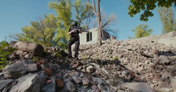 A soldier with a rifle walks through the ruins of a house and aims at the front — Wideo stockowe