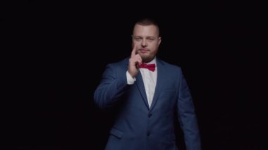 Mavi smokinli, kırmızı kravatlı zarif bir adam parmağını öne uzatıyor, gülümsüyor ve karanlığa dalıyor..