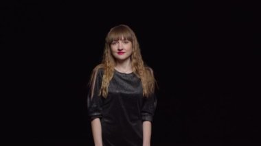 Koyu renk elbiseli, baştan çıkarıcı genç bir kadın siyah bir arka plan, moda ve cazibeyle poz verir ve kendini okşar.