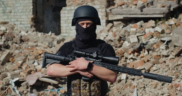 Tüfekli bir Ukraynalı asker yıkılmış bir evin arka planında duruyor ve etrafına bakıyor.