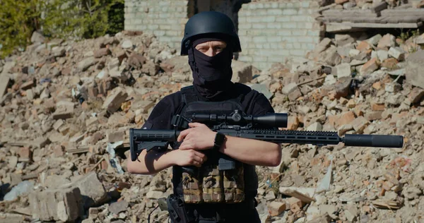 Tüfekli bir asker yıkılmış bir evin arka planına bakıyor..