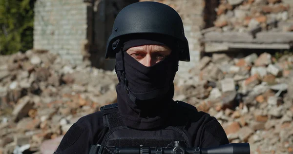 Silahlı bir asker, Ukrayna 'daki Rus saldırısından dolayı yıkılmış bir evin arka planında duruyor. Yakın plan..