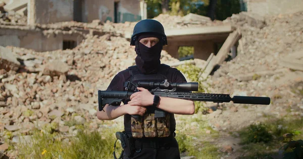 Tüfekli bir asker, savaş tarafından yıkılan bir evin arka planında duruyor. Orta boy.