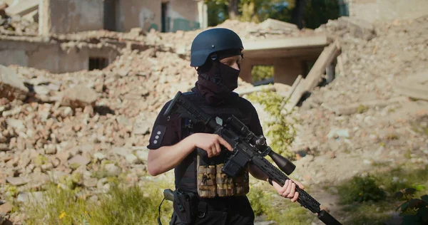 Tüfekli bir asker yıkılmış evin önünde duruyor ve etrafa bakıyor..