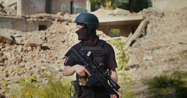 Tüfekli bir asker yıkılmış evin önünde duruyor ve etrafa bakıyor..