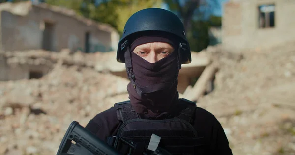 Yıkılan binanın arka planındaki bir asker başını çevirir, önüne bakar ve tüfeğini kaldırır. Yakın plan..