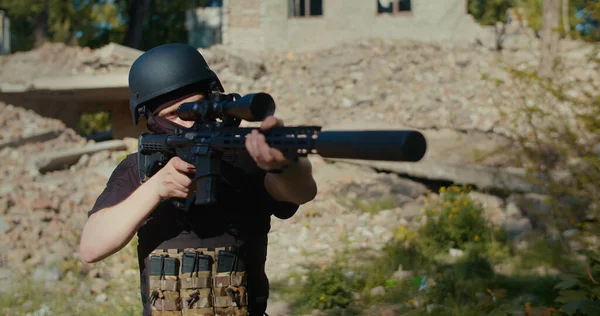Yıkılmış bir evin arka planında bir asker tüfeğini alır, nişan alır ve ateş eder. Orta boy..