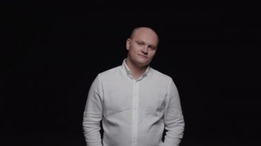 Beyaz gömlekli zarif kel bir adam kameraya bakıyor ve gülümsüyor..