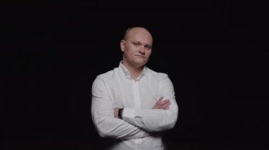 Zarif, kel bir adam önüne bakar ve siyah bir arka planda kameraya poz verir..