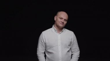 Beyaz gömlekli kel bir adam siyah arka planda kameraya poz veriyor..