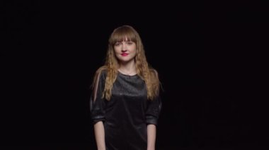 Koyu renk elbiseli, baştan çıkarıcı genç bir kadın siyah bir arka plan, moda ve cazibeyle poz verir ve kendini okşar..