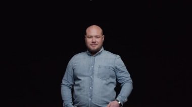 Kel bir adam sakalını okşar ve siyah arka planda kameraya poz verir..