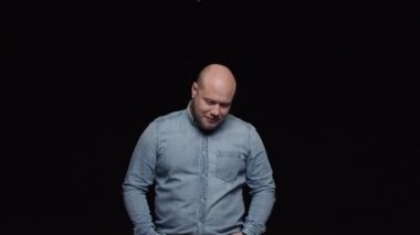 Kel ve sakallı bir adam başını öne kaldırır ve siyah arka plana karşı olumlu bir şekilde başını sallar..