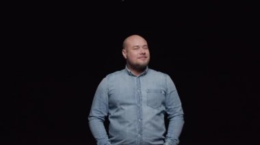 Kot gömlekli sakallı kel bir adam öne bakıp gülümsüyor. Bir adam kameranın önünde siyah bir arkaplanda poz veriyor.