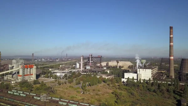 Metallorjik bir bitkinin arka planında siyah dumanla tüten beyaz bulutlu mavi gökyüzü. Demir ve çelik üretimi. Çevre kirliliği.