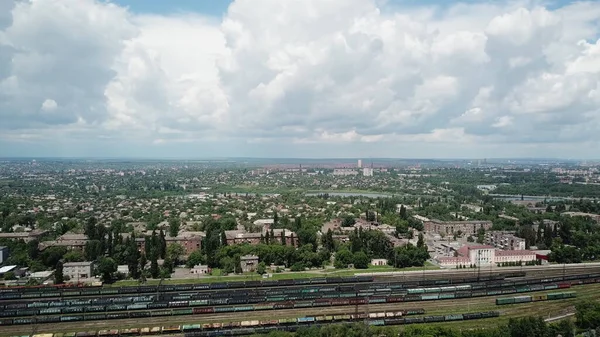 Arabalı tren istasyonu manzarası. Şehrin üzerinde büyük blokları olan mavi bir gökyüzü. Lojistik sektörü, nakliye işi konsepti. İHA yüksek açı görüntüsü taraması.