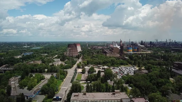 Buharı tüten bir metallorjik bitkinin arka planında beyaz bulutlu mavi gökyüzü. Demir ve çelik üretimi. Çevresel etki. İHA yüksek açı görüntüleme