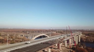 Yol boyunca giden ve malları taşıyan arabalarla dolu bir köprünün havadan çekilmiş görüntüsü. Nehrin üzerinde bir köprüden uçmak, otoyolda arabalarla hareket etmek. Doğanın sahne sahnesi. Yan görünüm.