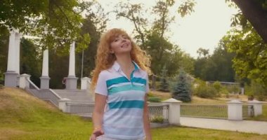 Sunny Park 'taki genç kadın. Beyaz bir bayan şarkı söylüyor ve eğleniyor. Müzik, doğa, yaşam tarzı konsepti. Parkta gün batımında şarkı söyleyen kadın.