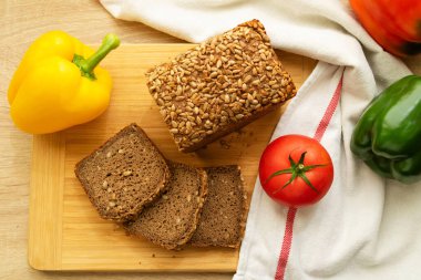 Düz dilimlenmiş çavdar ekmeği, ayçekirdeği, domates ve biber ile ahşap masada yatıyordu..