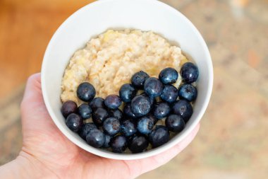 Evde yemek pişir. Elinde yulaf ezmesi ve yaban mersini tabağı.