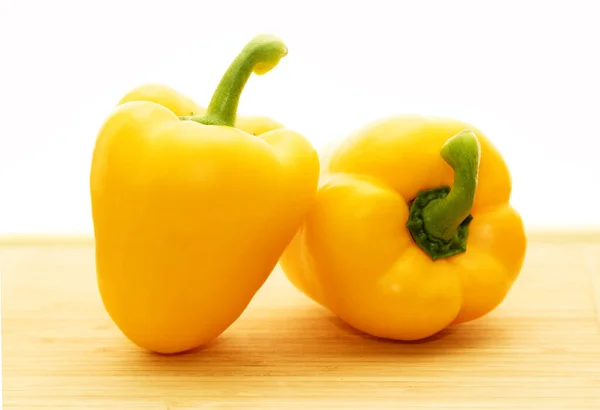 Two yellow peppers on a wooden table, isolated on a white background.