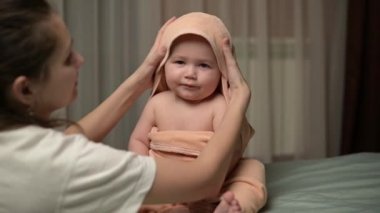 A young woman dries her son with a towel after a bath