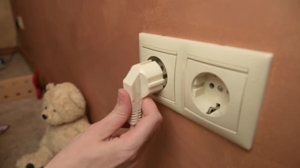 Young woman inserts the plug of the electrical appliance into the socket — Vídeos de Stock