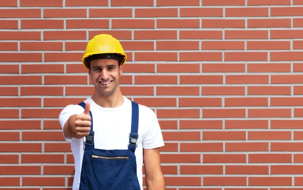 Giovane lavoratore mostrando tumb davanti a un muro di mattoni — Foto Stock