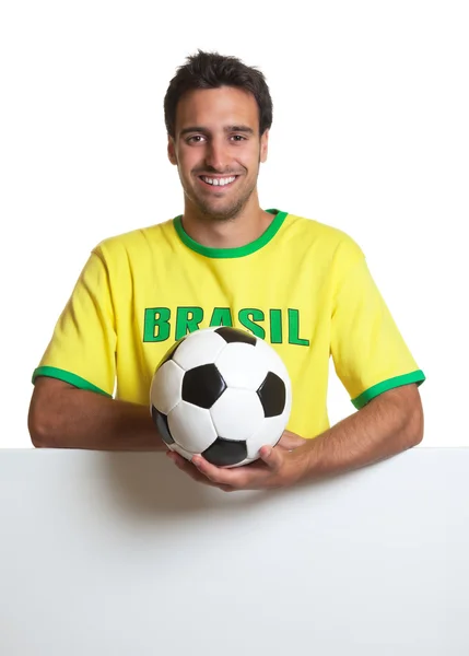 Смеющийся бразильский футбольный фанат с мячом за вывеской — стоковое фото
