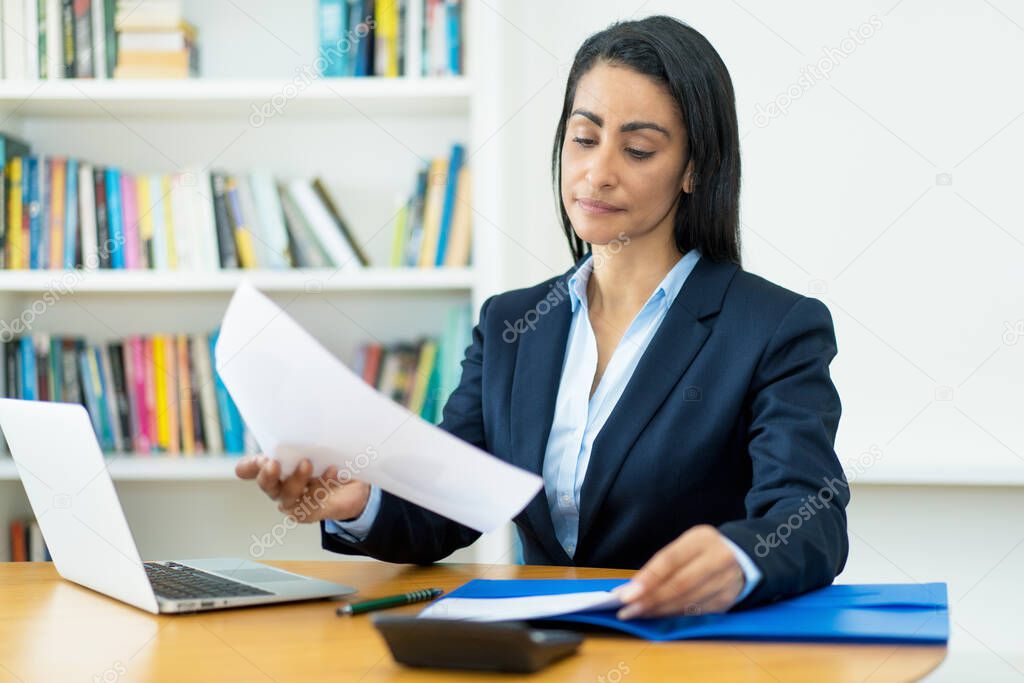 Hispanic mature businesswoman working with documents at desk at office