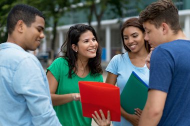 Beyaz ve Latin Amerikalı erkek ve bayan öğrencilerden oluşan bir grup açık havada yapılan çalışmalar hakkında konuşuyor.