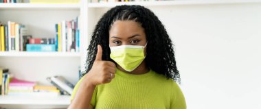 Covid-19 virüsünden korunmak için yeşil maskeli iyimser Afro-Amerikalı kadın.