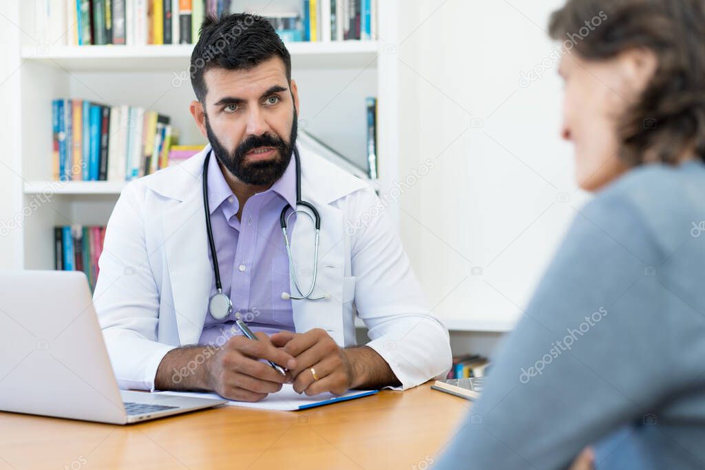 Concerned mature doctor with hipster beard talking with patient at office of hospital