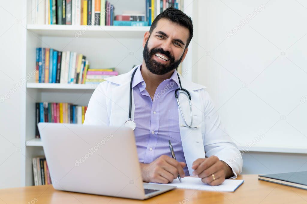 Portrait of happy laughing latin american mature doctor with hipster beard at office of clinic