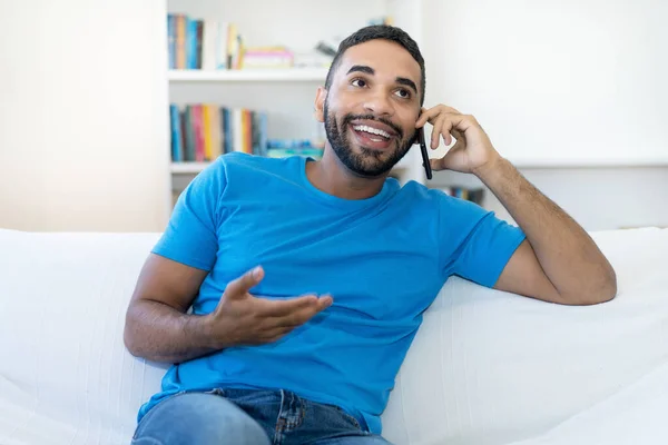 Handsome latin american hipster man with beard flirting at mobile phone indoors at home