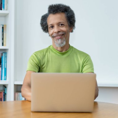 Yakışıklı Afrikalı Amerikalı adam evdeki masadaki bilgisayardan online alışveriş yapıyor.