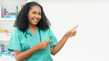 Latin american medical student or female nurse pointing sideways at clinic clipart