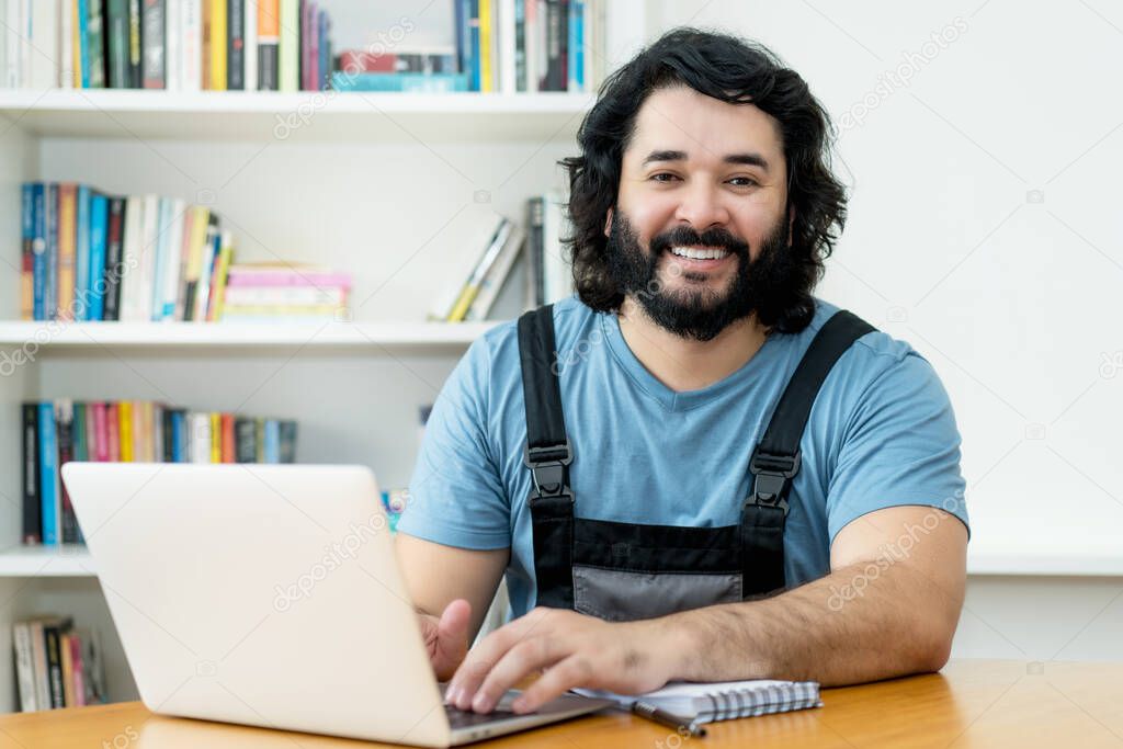 Laughing handyman with beard working at computer at desk at office