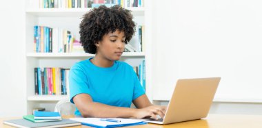 Ciddi Afrikalı Amerikalı kız öğrenci evdeki masada bilgisayar öğreniyor.