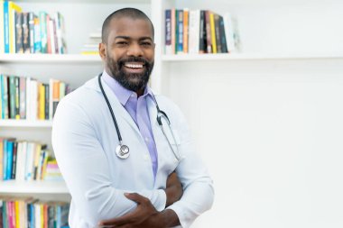 Hastanenin ofisinde sakallı ve steteskoplu gülen Afrikalı Amerikalı doktor.