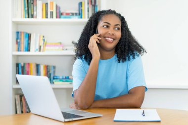 Latin Amerikalı bir kadın telefonda erkek arkadaşıyla konuşuyor. Evdeki masada.