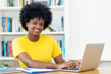 Oldukça Afrikalı Amerikalı kız öğrenci evdeki masada bilgisayar alışverişi yapıyor.