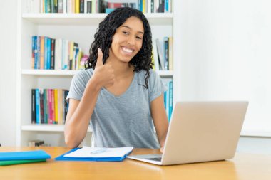 Başarılı Güney Amerikalı kız öğrenci üniversitenin masasında baş parmağını gösteriyor.