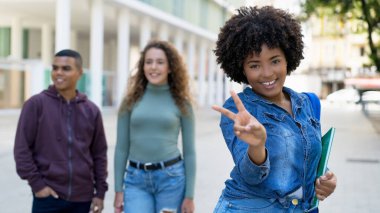 Happy african american female student with backpack and group of international students outdoor in summer in city