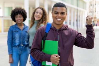 Motivated latin american male student with backpack and group of international students outdoor in summer in city