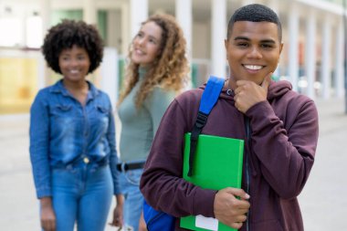 Handsome latin american male student with backpack and group of international students outdoor in summer in city