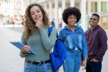 Laughing german female student with backpack and group of international students outdoor in city in summer